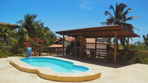 Ein Pool mit gewölbter Kante, umgeben von Palmen und einer überdachten Sitzgelegenheit.