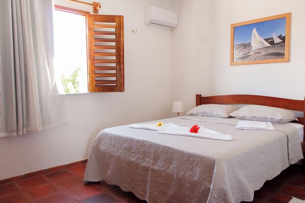 Una cama bien hecha con una colcha blanca, un cabecero de madera y un cuadro de veleros en la pared.