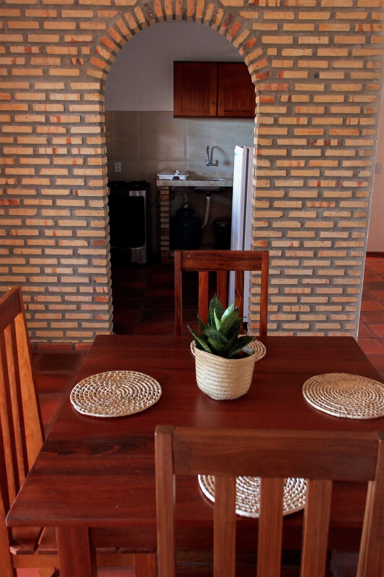 Un comedor con pared de ladrillo, mesa de madera, sillas y una planta en maceta.