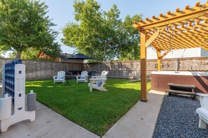 En trädgård med en pergola av trä, ett bubbelbad och utomhusmöbler.