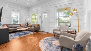 A spacious living room with a wooden floor, a large sofa set, a coffee table, and a round rug. There are two large windows with white shutters, and a ceiling fan is visible. - ONLY 4 BLOCKs to Magnolia-Hot tub-Texas Bell in Waco (Waco)