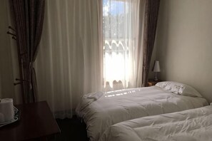 A hotel room with two beds, a window with curtains, a bedside table with a lamp, and a small table with a tray. - Te Puia Hot Springs Hotel (Te Puia Springs)