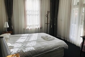 A hotel room with a bed, a nightstand, a lamp, and sheer curtains. - Te Puia Hot Springs Hotel (Te Puia Springs)