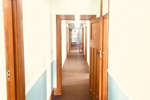 A long, narrow hallway with wooden doors on both sides, leading to a room at the end. - Te Puia Hot Springs Hotel (Te Puia Springs)