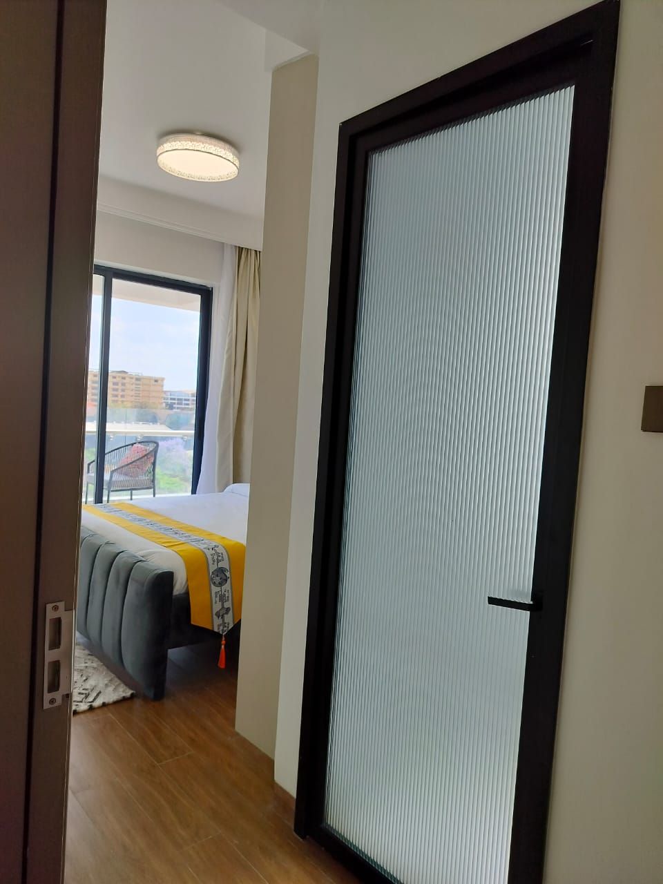 Een hotelkamer met een groot raam, een bed met een gele en witte dekbedovertrek, en een schuifdeur.