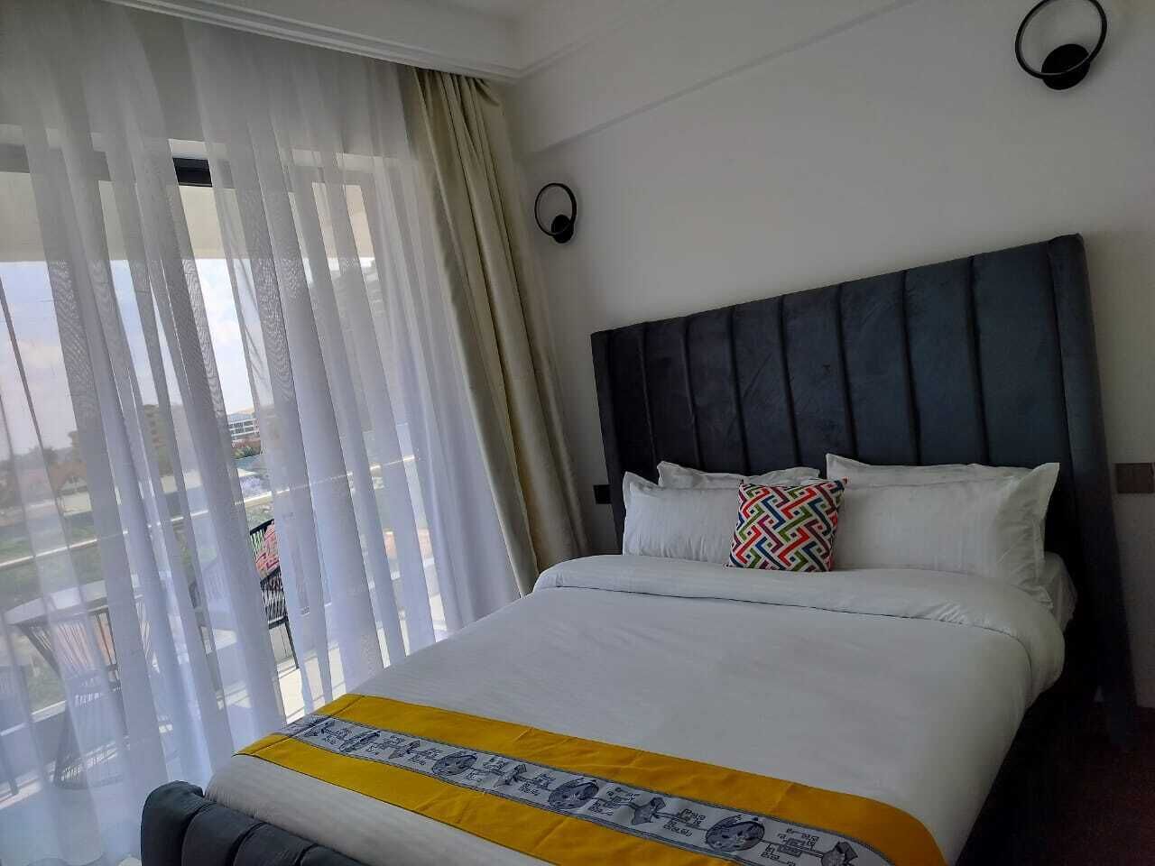 A hotel room with a bed, curtains, a headboard, and a view of the outside.