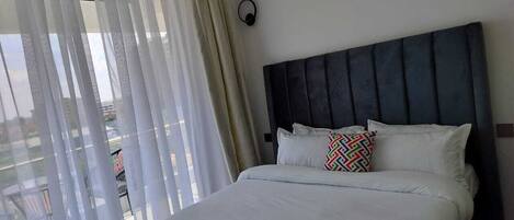 A hotel room with a bed, curtains, a headboard, and a view of the outside.