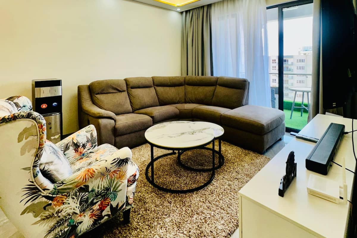 A modern living room with a sectional sofa, a round coffee table, a flat-screen TV, and a small desk with a computer.