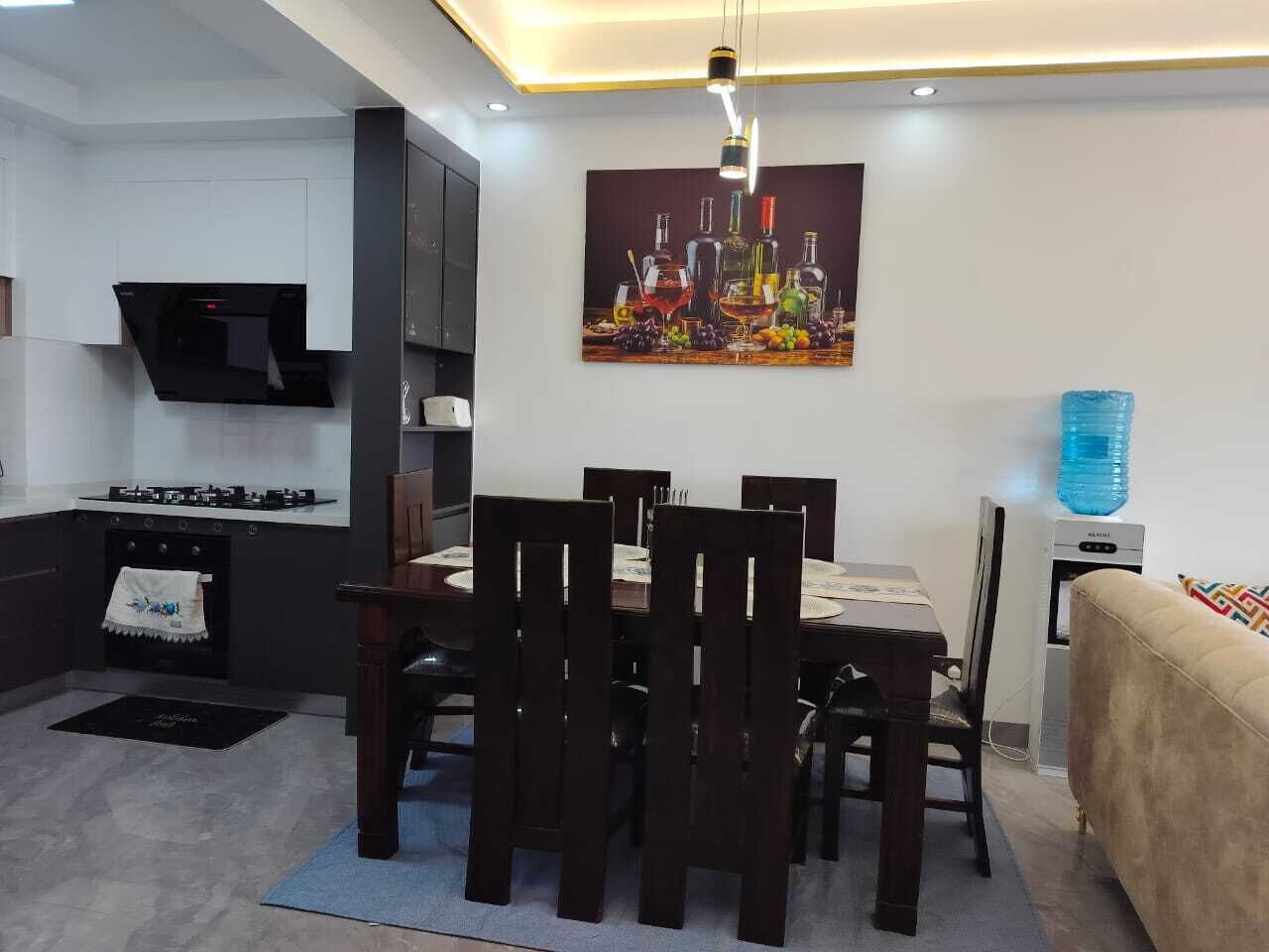 A modern kitchen with a dining area, featuring a table with chairs, a water dispenser, and a painting on the wall.