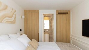 Una habitación de hotel moderna con una cama grande, un armario de madera, un baño con lavamanos y un televisor en la pared.