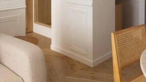 Una habitación con paredes blancas, suelo de madera y una silla de mimbre.