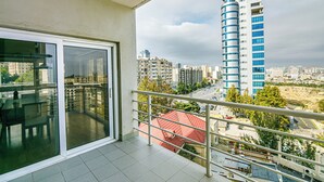 En balkon med glasdør, gelænder og udsigt over et bybillede med høje bygninger.