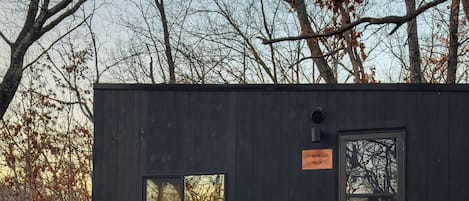 A cabin with a small deck, two Adirondack chairs, a fire pit, and a sign reading "Dominico."