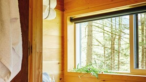 A wooden cabin bathroom with a toilet, a window with a view of trees, and a towel hanging on the wall. - Postcard Cabins St Francois, Outdoor Collection by Marriott Bonvoy (French Village)