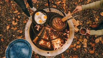 A fire pit with food being cooked, surrounded by people.