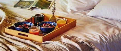A bedroom with a bed, a wooden headboard, a window with a view of greenery, and a tray with breakfast items.