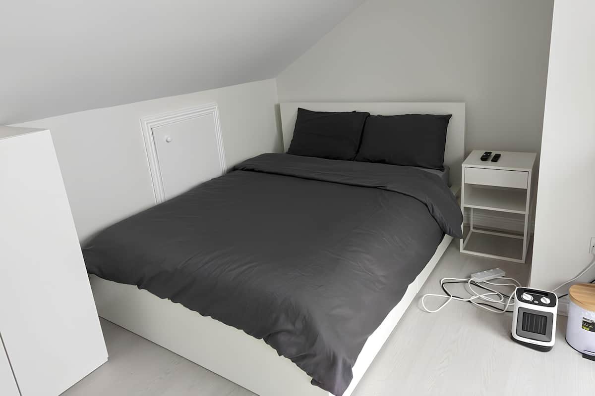 A modern, minimalist bedroom with a single bed, white wardrobe, and a bedside table with a heater.