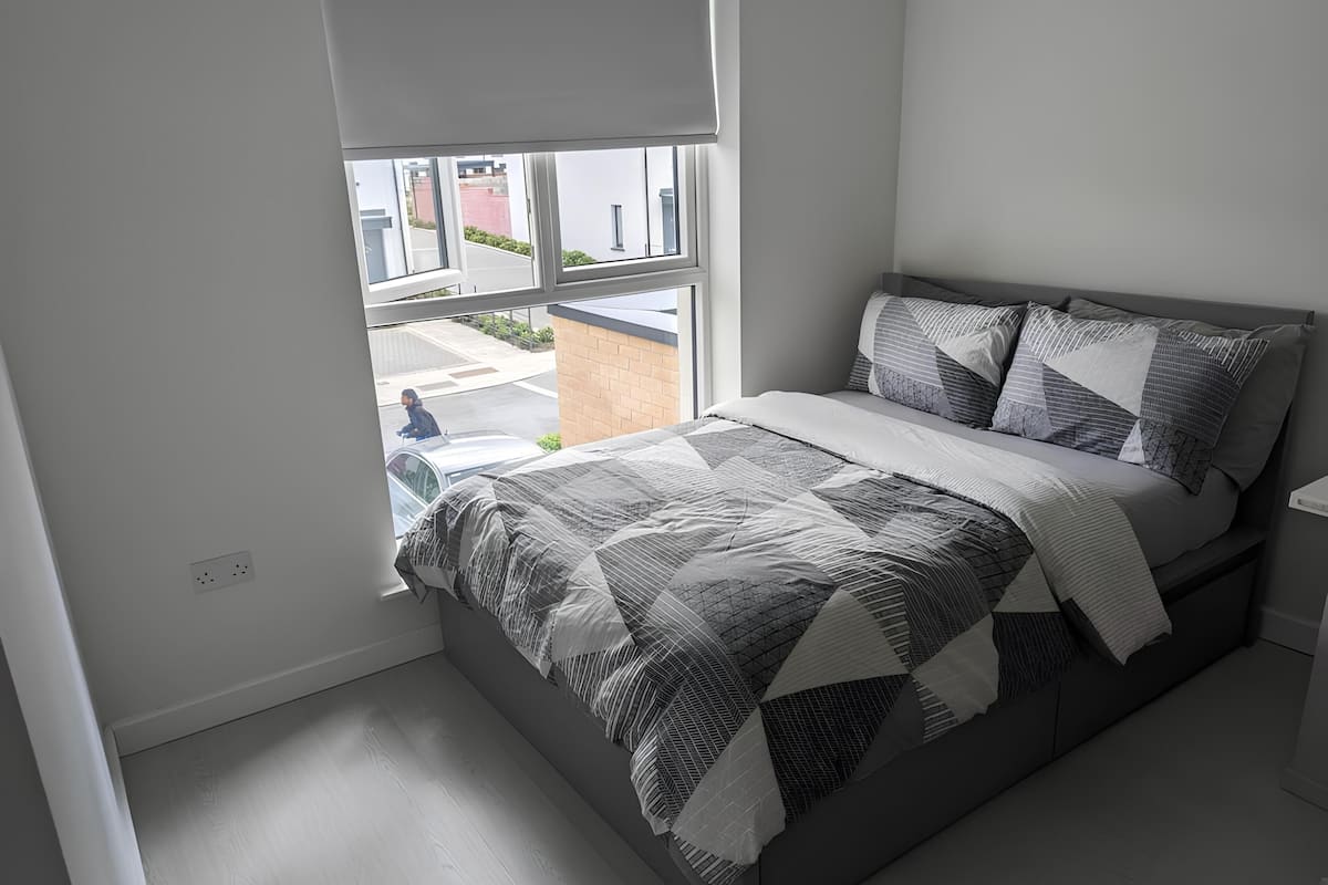 A bedroom with a bed, a window, and a view of the street.