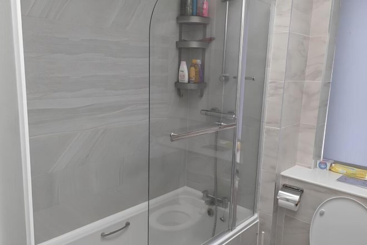 A modern bathroom with a glass-enclosed shower, a toilet, and a small shelf with toiletries.