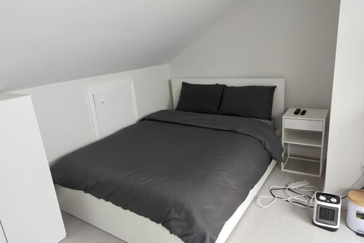 A modern, white bedroom with a bed, a nightstand, and a small heater.