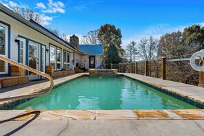 A swimming pool with a stone deck, a wooden deck with a railing, and a building with large windows and a stone chimney. - Paradise Springs is just that, paradise! (SEVIERVILLE)