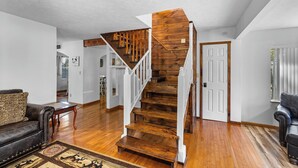Ein geräumiger Wohnbereich mit einer Holztreppe, einem Ledersofa und einem gemusterten Teppich.