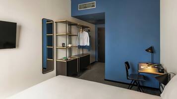 Ein Hotelzimmer mit einem Bett, einem Schreibtisch mit Stuhl, einem Kleiderschrank, einem Spiegel und einem Fernseher.