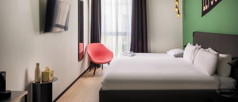 A hotel room with a bed, a chair, a TV, and a wall with a message.