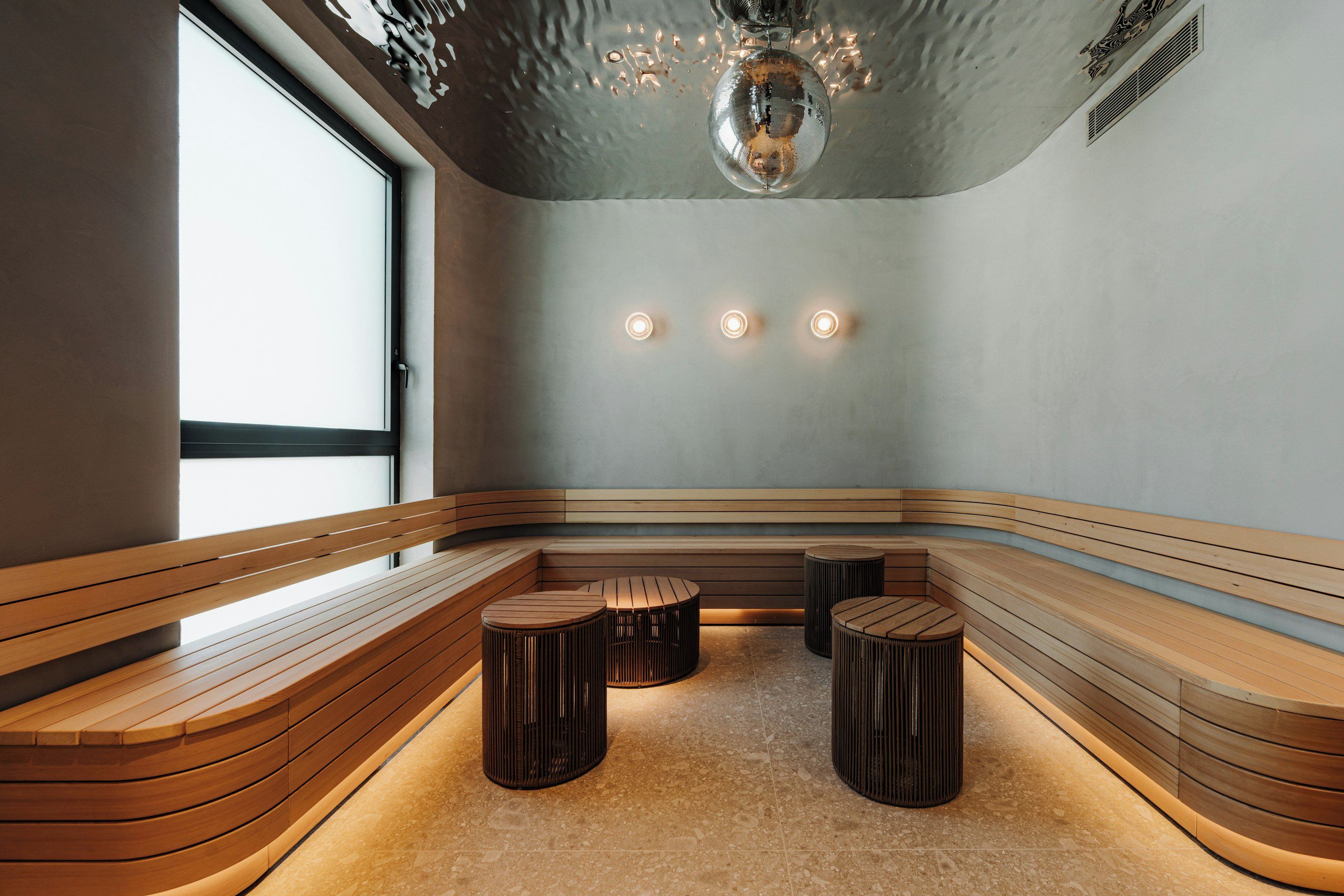 A modern interior with a curved wooden bench seating area, a ceiling with a decorative element, and three wall-mounted lights.
