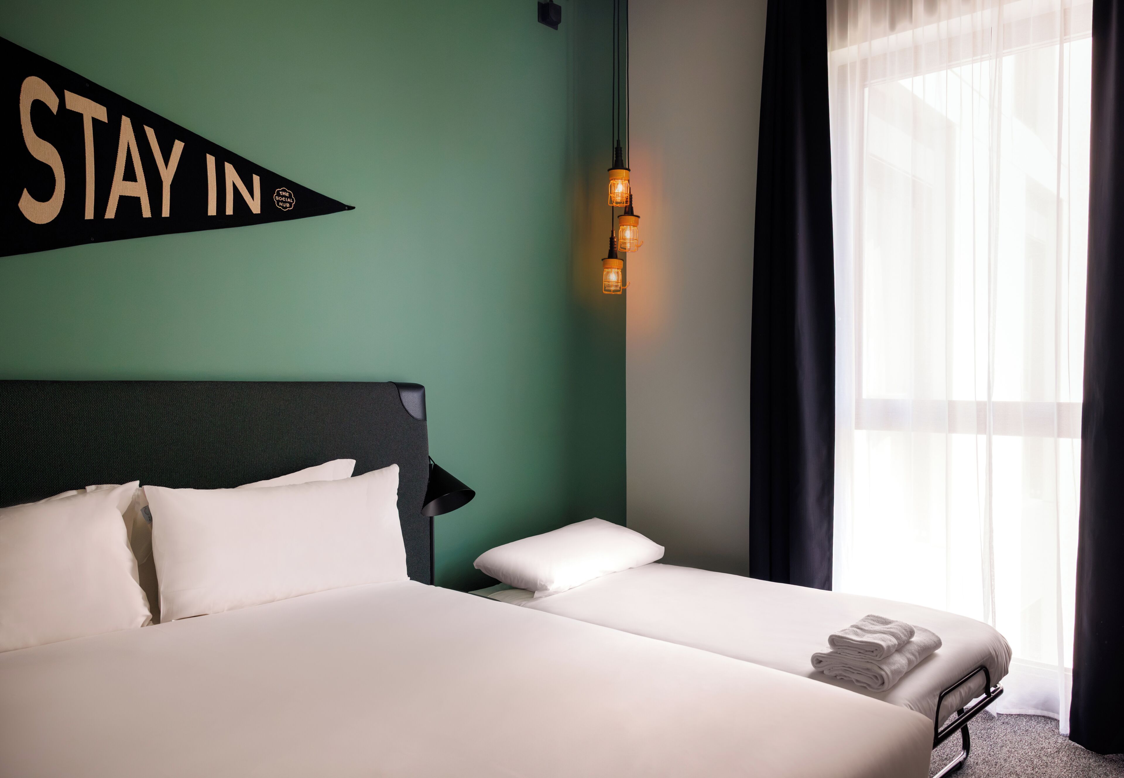 A hotel room with a bed, a wall-mounted sign, a lamp, and a window with curtains.