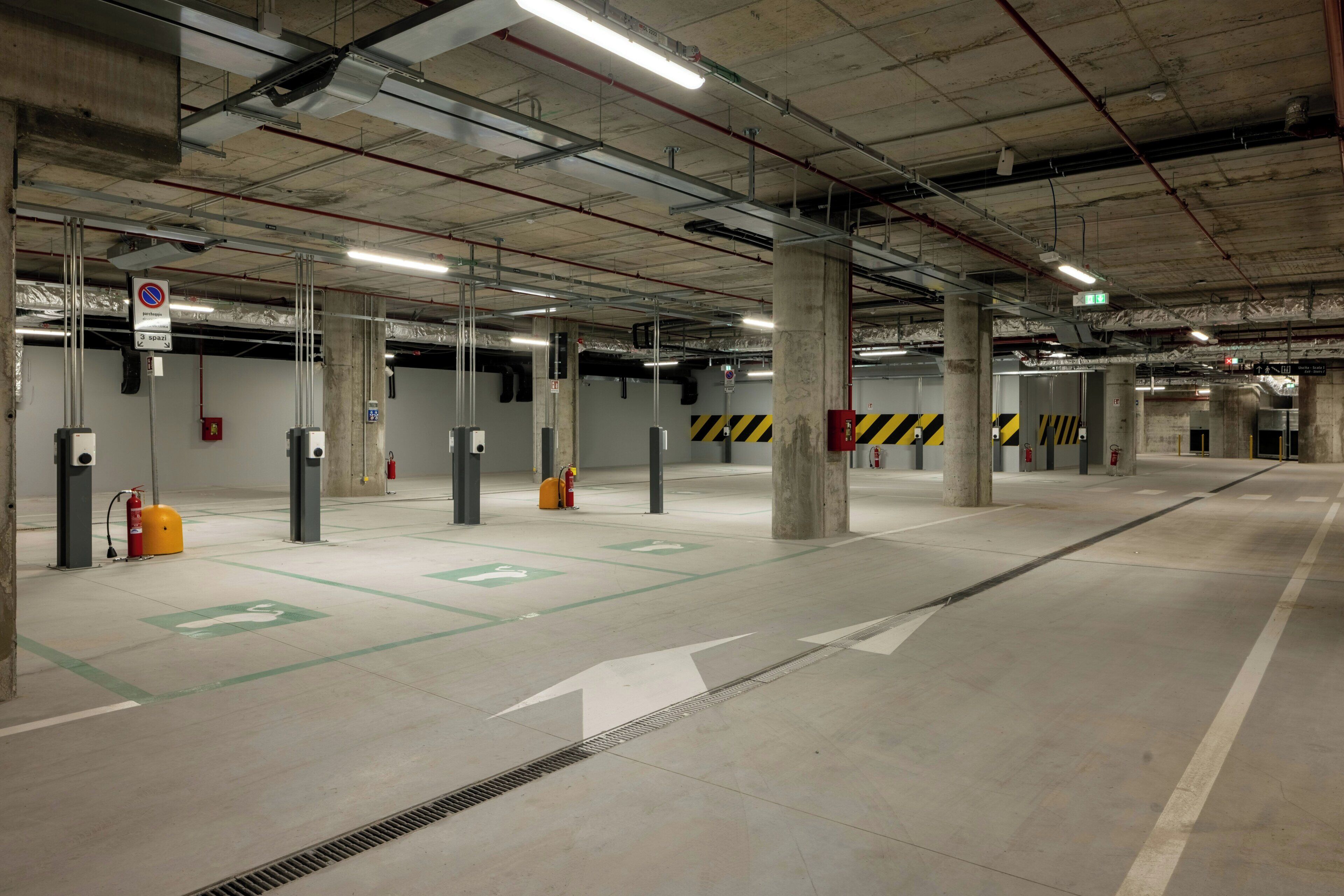 Een parkeergarage met betonnen pilaren, pijlen die de richting aangeven en brandblussers.