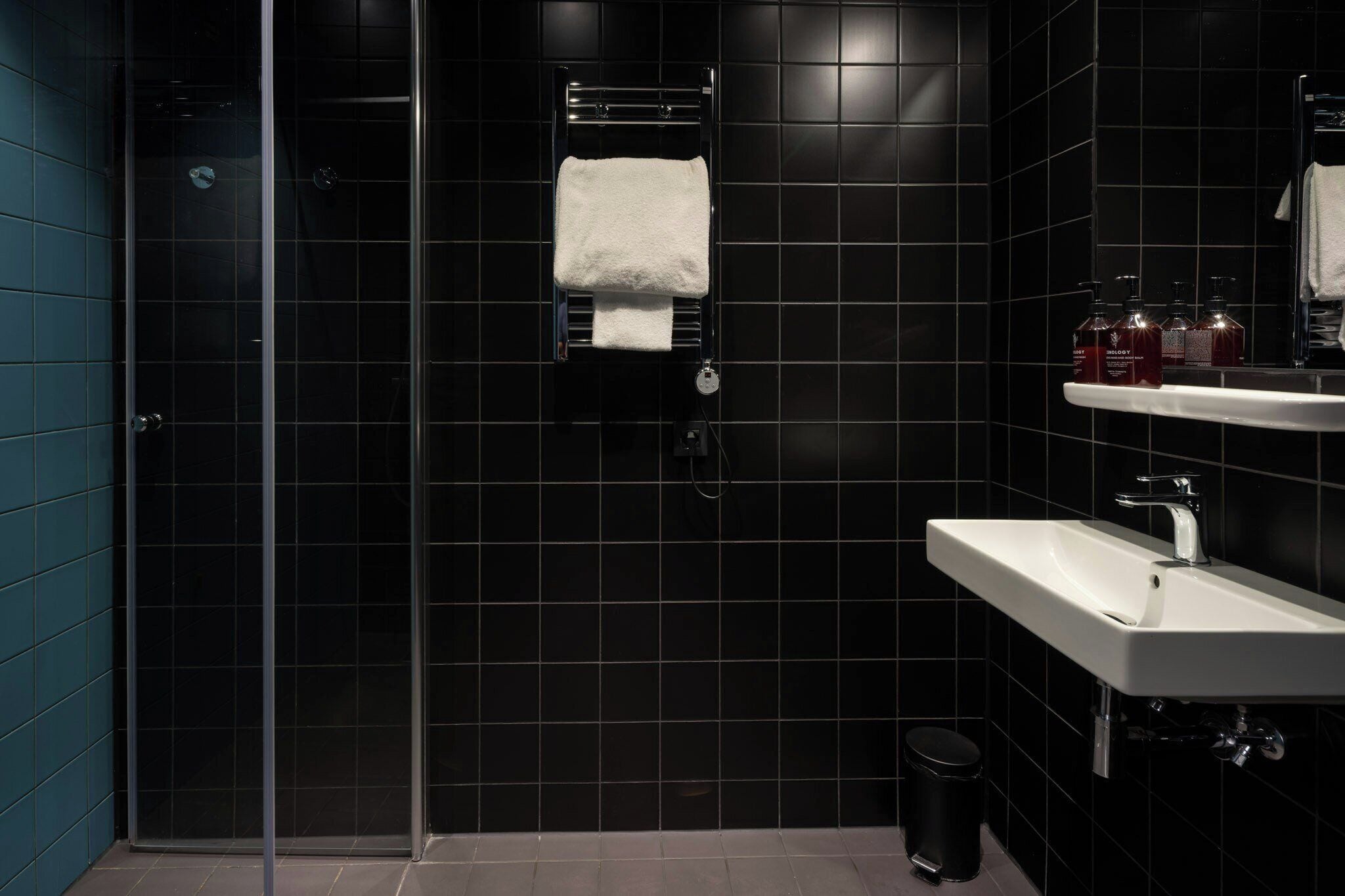 Un baño moderno con cabina de ducha de vidrio, un lavabo blanco y un cubo de basura negro.
