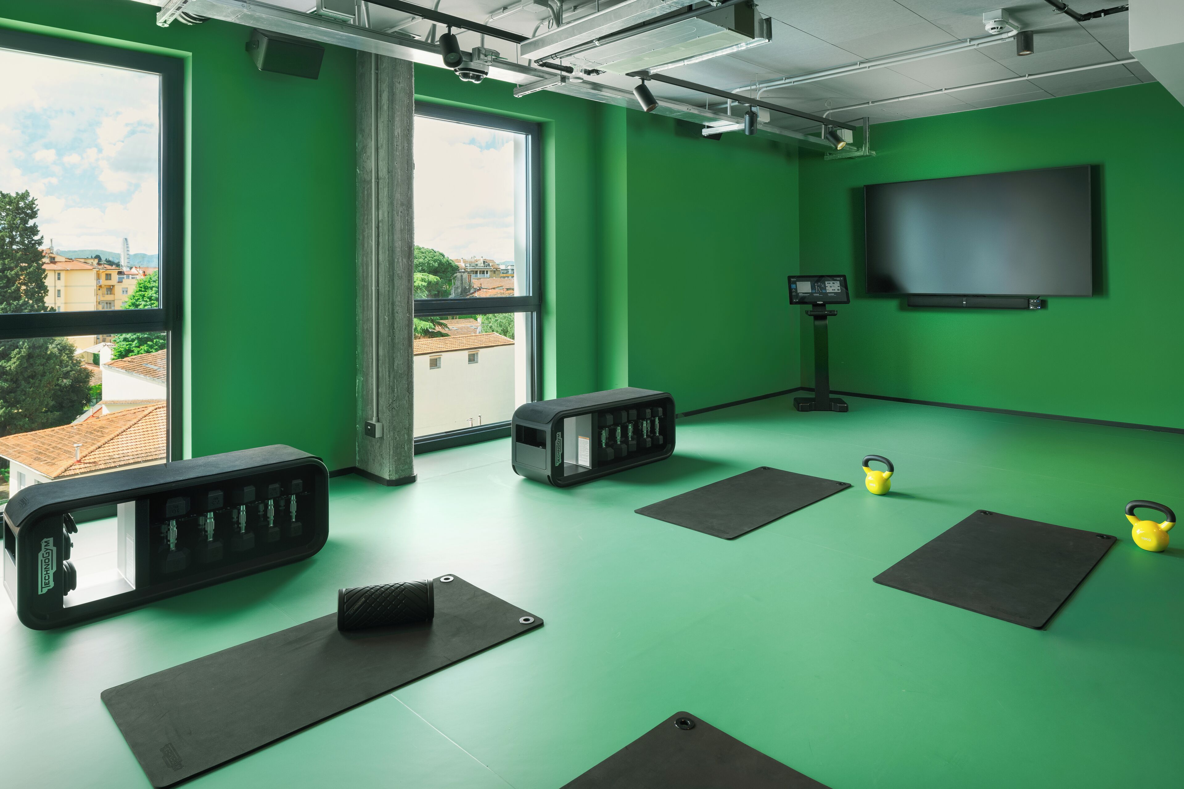 Een groene kamer met een groot raam, een flatscreentelevisie en fitnessmatten.