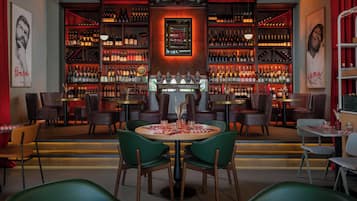Un bar doté de plusieurs étagères remplies de bouteilles, d’un élément décoratif central et de coins salon avec des tables et des chaises.