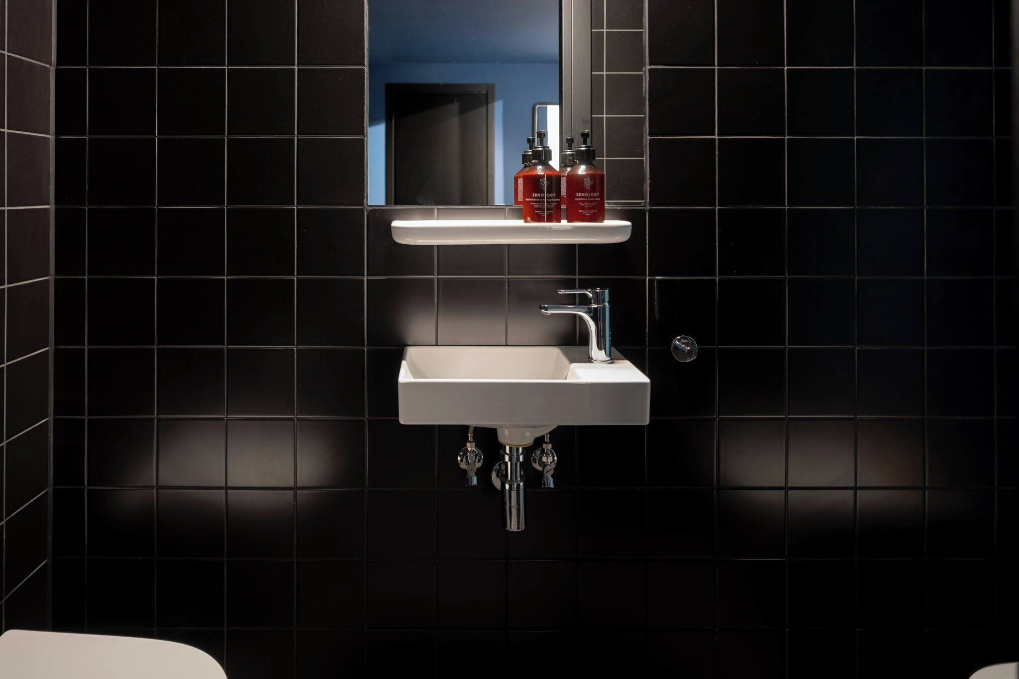 A bathroom with a white sink, chrome faucet, and black tiled walls.