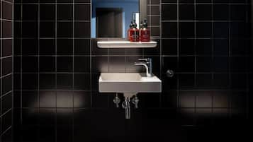 A bathroom with a white sink, chrome faucet, and black tiled walls.