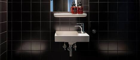 A bathroom with a white sink, chrome faucet, and black tiled walls.