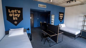 Habitación de hotel con dos camas, un escritorio y una litera. Hay dos carteles que dicen 'Quédémonos'.