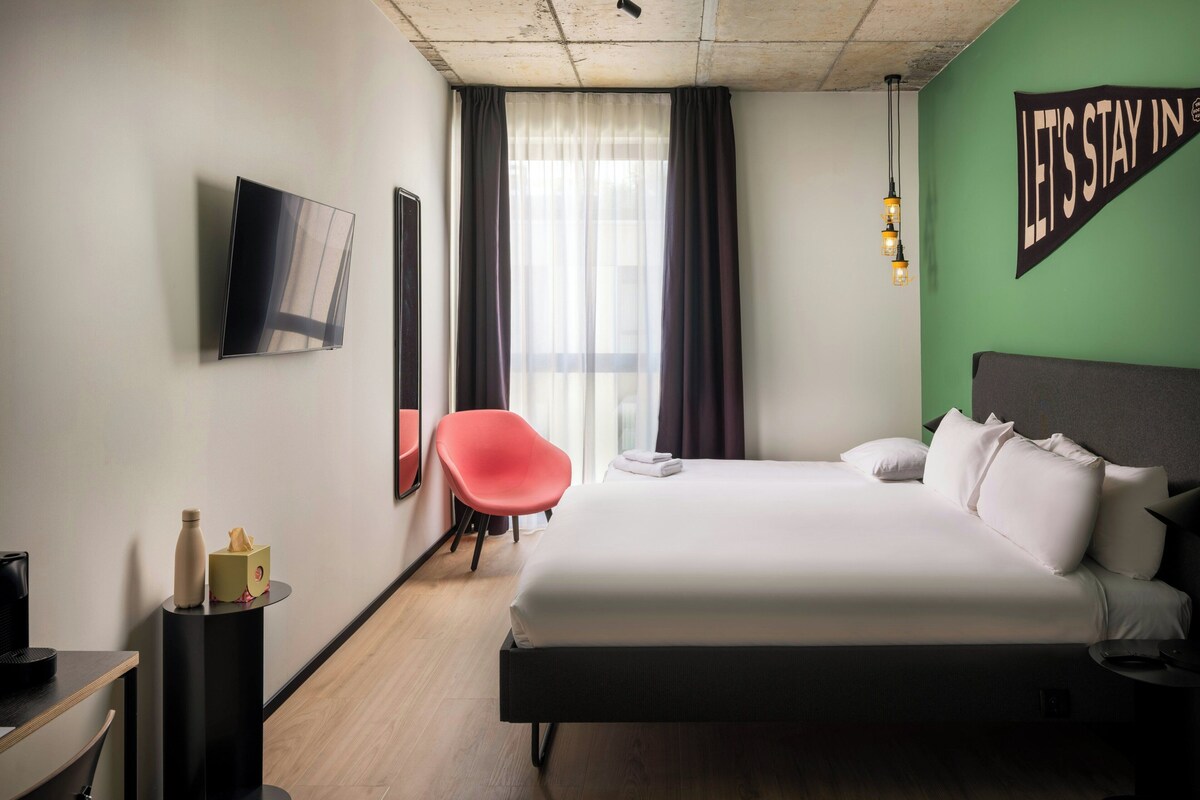 Habitación de hotel con cama, una silla, un televisor y un cartel que dice 'LET'S STAY IN'.