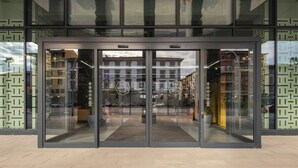 Entrada de un edificio moderno con puertas de vidrio, reflejando la calle, y un letrero que dice 'The Social Hub'.