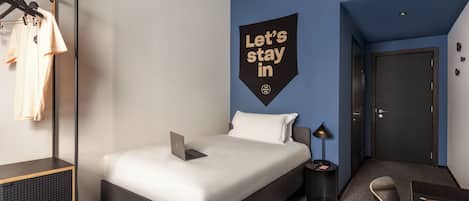 Una habitación de hotel moderna con una cama, un escritorio, una silla, un armario y un cartel en la pared.
