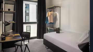 A hotel room with a bed, a desk with a chair, a wardrobe, and a window with curtains.