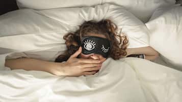 A person lying in bed with a white pillow and a black eye mask.