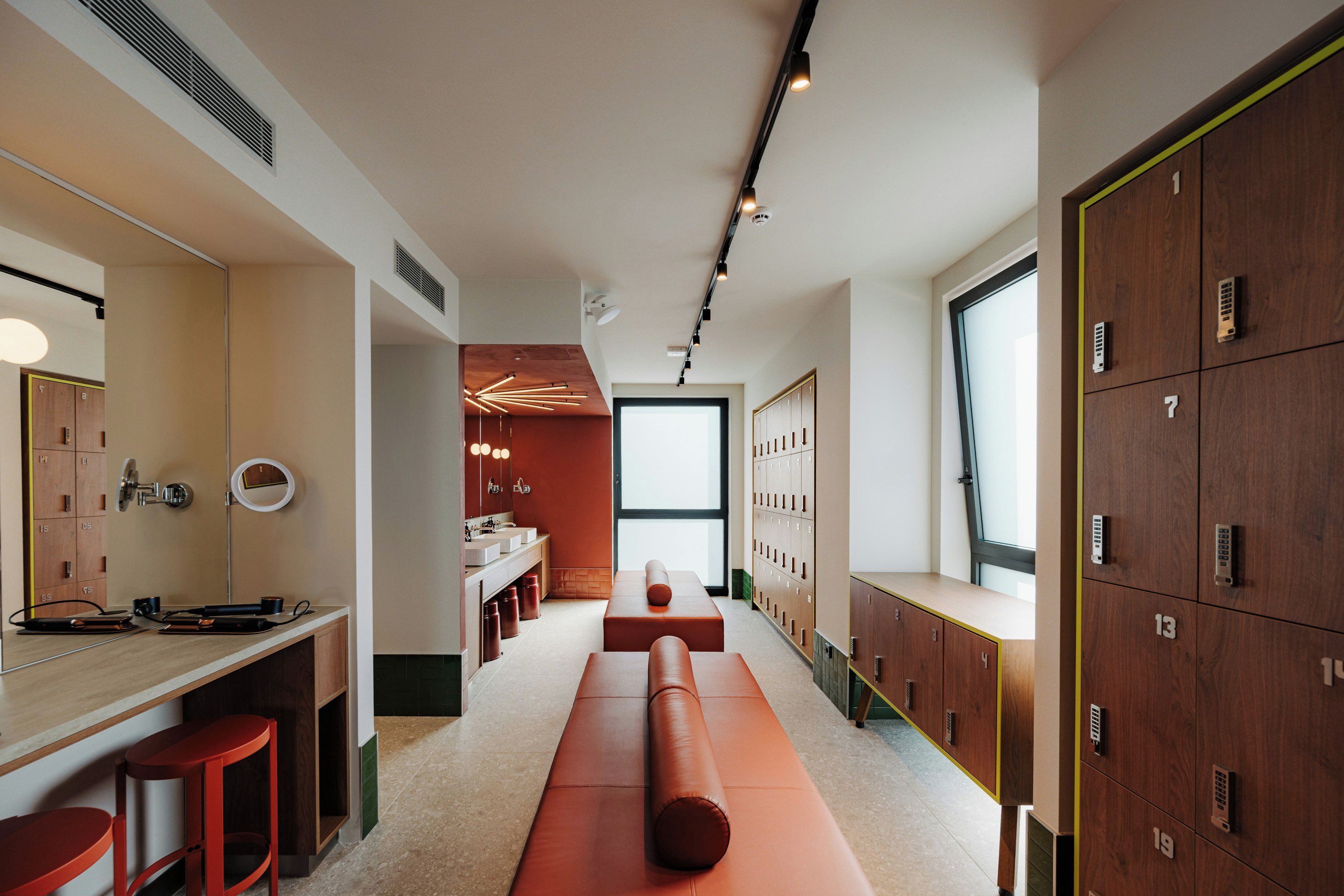 A modern bathroom with a long bench, lockers, and a vanity with a mirror.