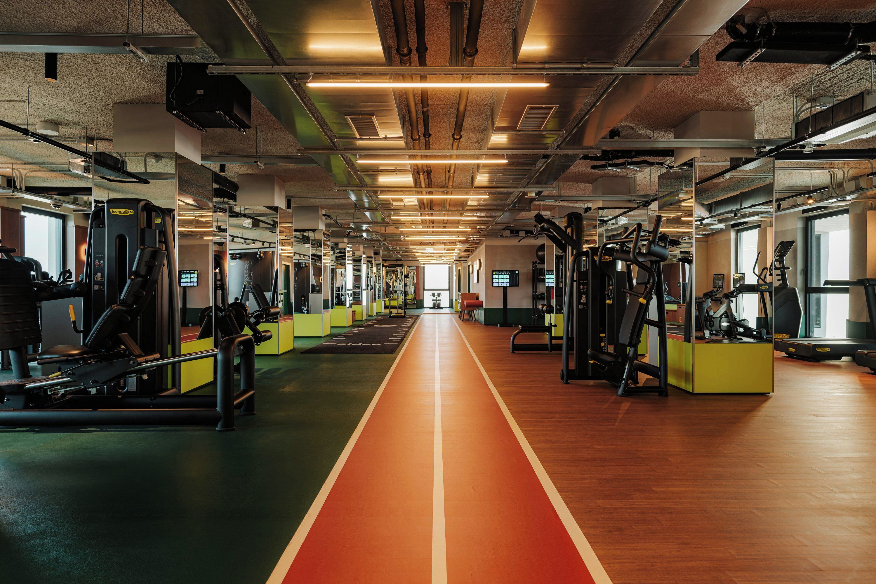 A gym with exercise equipment, a central running track, and multiple monitors on the walls.