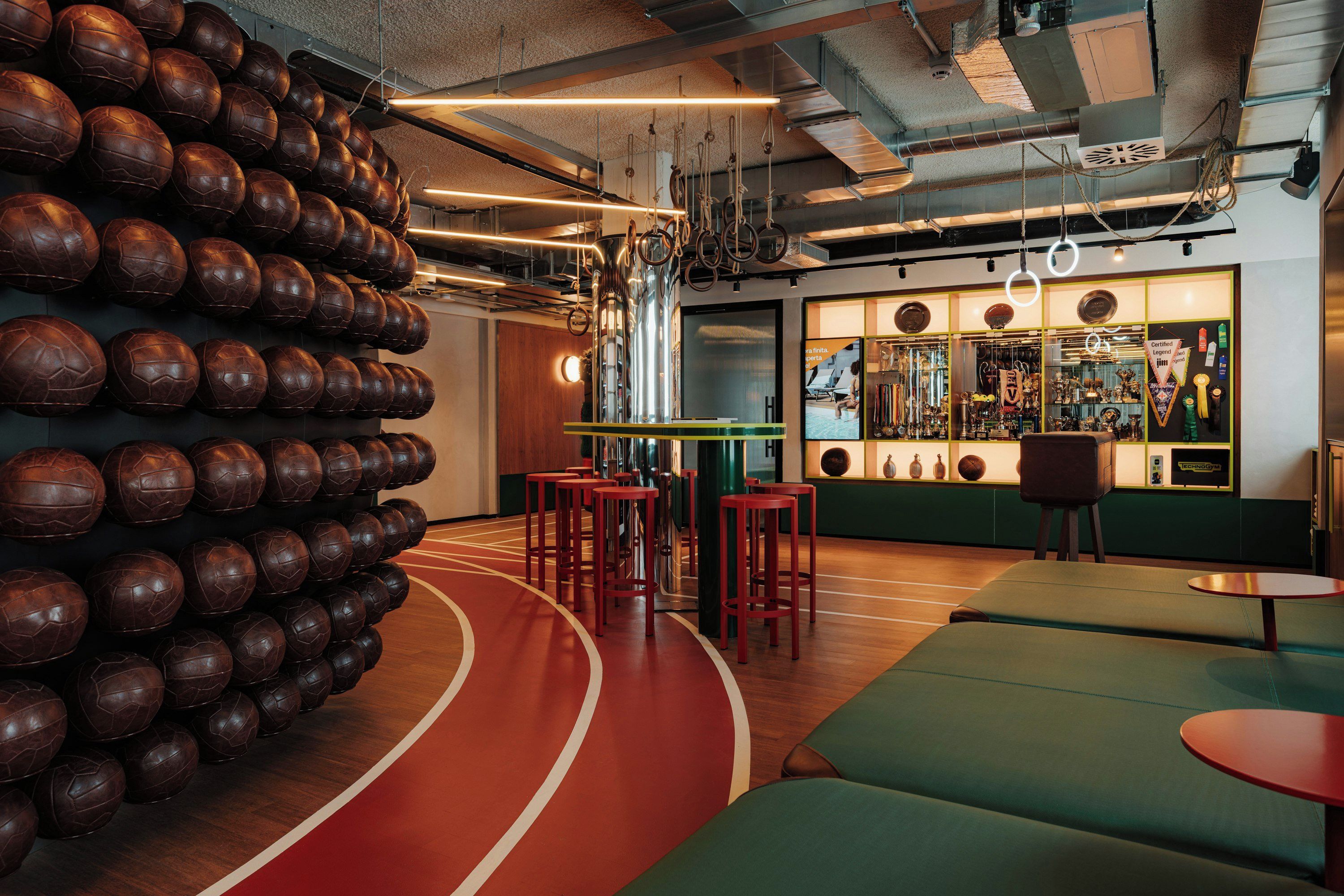 Un salon à thème sportif, avec un mur décoré de ballons en cuir, des tabourets de bar rouges et un espace bar agrémenté de trophées.
