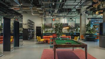 Een moderne loungeruimte met een pooltafel, comfortabele zitplaatsen en diverse planten.