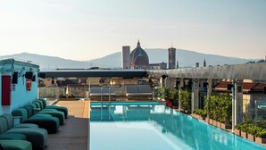 Una piscina en la azotea con sillones de descanso, vista despejada de un edificio con cúpula y montañas al fondo.