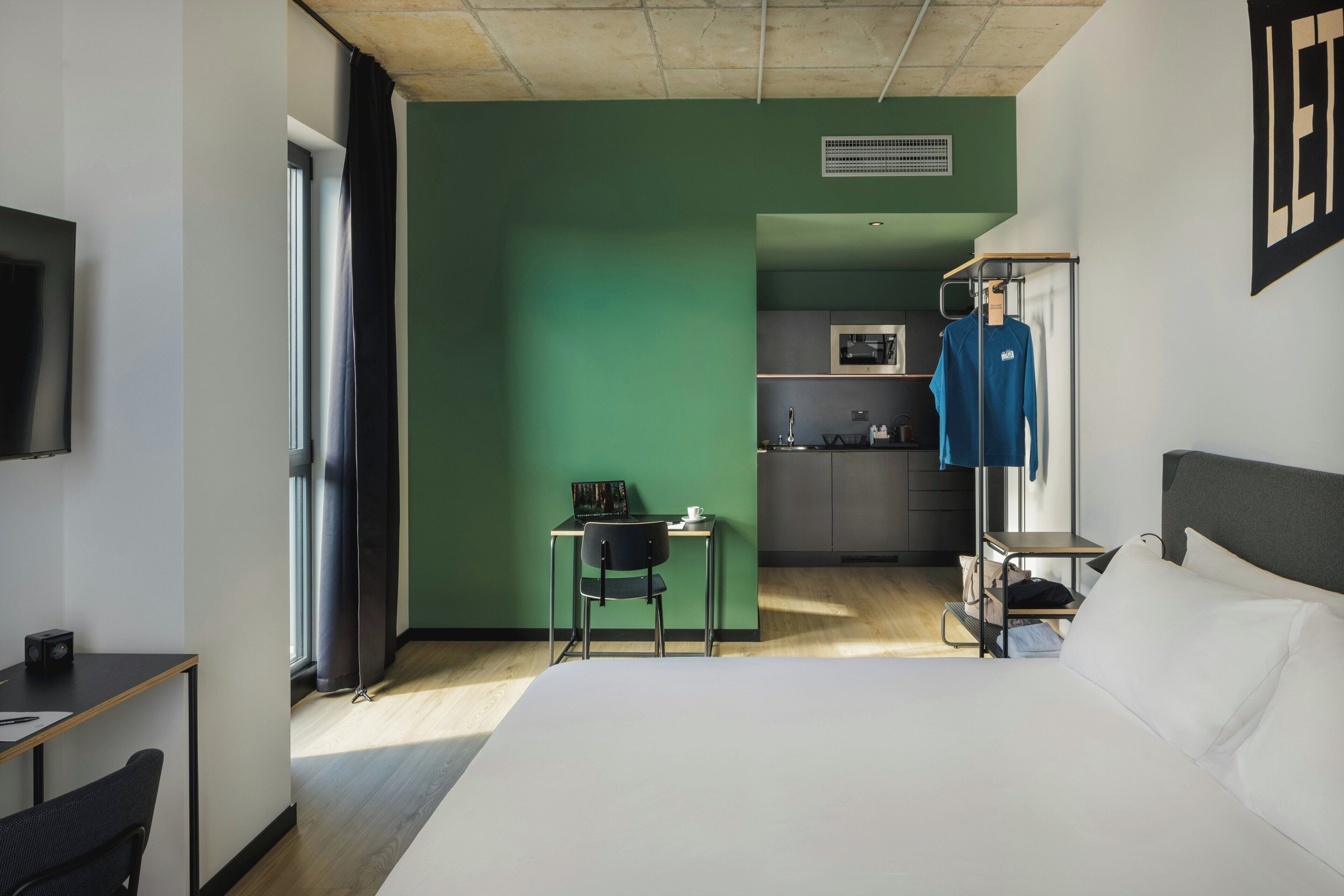 Een hotelkamer met een bed, een bureau, een stoel, een kitchenette en een tv aan de muur.