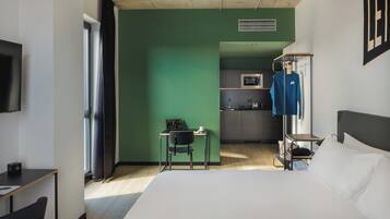 Une chambre d’hôtel équipée d’un lit, d’un bureau, d’une chaise, d’une télévision, d’une kitchenette et d’une armoire.